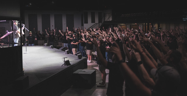 Men leading worship: a guitar on stage, brothers with hands raised in a darkened sanctuary.